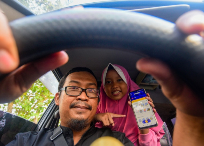 Seorang anak menunjukkan aplikasi Travoy kepada ayahnya di perbatasan Kabupaten Grobogan - Sragen, Jawa Tengah, Rabu (15/4/2026). PT Jasa Marga (Persero) Tbk meluncurkan aplikasi Travoy sebagai bagian dari komitmen transformasi layanan digital untuk memudahkan para pengguna jalan tol di Indonesia. (Achmad Fazeri/Disway Jateng)