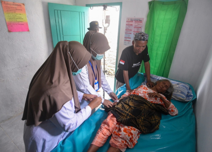 TINDAKAN MEDIS: Dua bidan, Indah Milasari dan Fatimah, didampingi oleh perangkat desa setempat memasang infus pada tangan, Mamah, sebelum dirujuk ke puskesmas Pulau Sapeken, yang memiliki perlengkapan maupun tenaga medis lebih memadai, Selasa, 3 Juni 2025. (Achmad Fazeri/Disway Jateng)